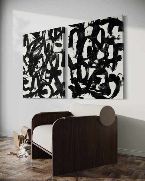 two black and white paintings on a wall above a bed
