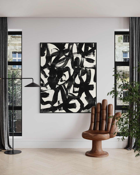 a black and white painting hanging on a wall next to a chair