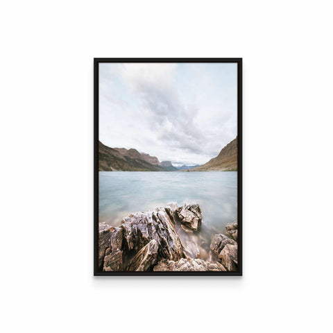 a picture of a rocky beach with water and mountains in the background